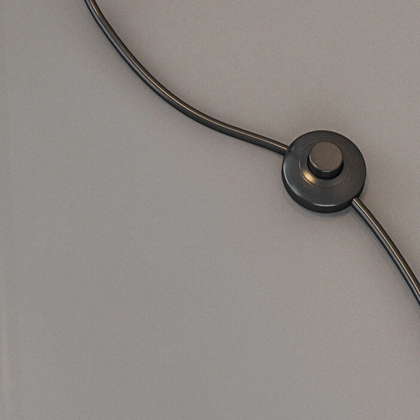 A close-up of the black foot switch and power cord for the Minimalist LED Arc Floor Lamp, resting on a smooth grey surface.