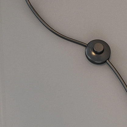 A close-up of the black foot switch and power cord for the Minimalist LED Arc Floor Lamp, resting on a smooth grey surface.