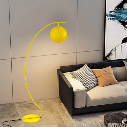 A yellow minimalist LED arc floor lamp with a spherical shade, casting a warm glow next to a modern sofa in a contemporary living room.