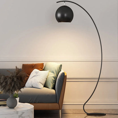 Minimalist black LED arc floor lamp with an adjustable spherical head, casting a warm light over a grey and brown sofa in a modern living room.