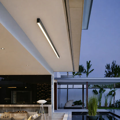 A minimalist linear LED ceiling light mounted on the outdoor patio ceiling of a modern home, illuminating the space at dusk with a warm, even glow.