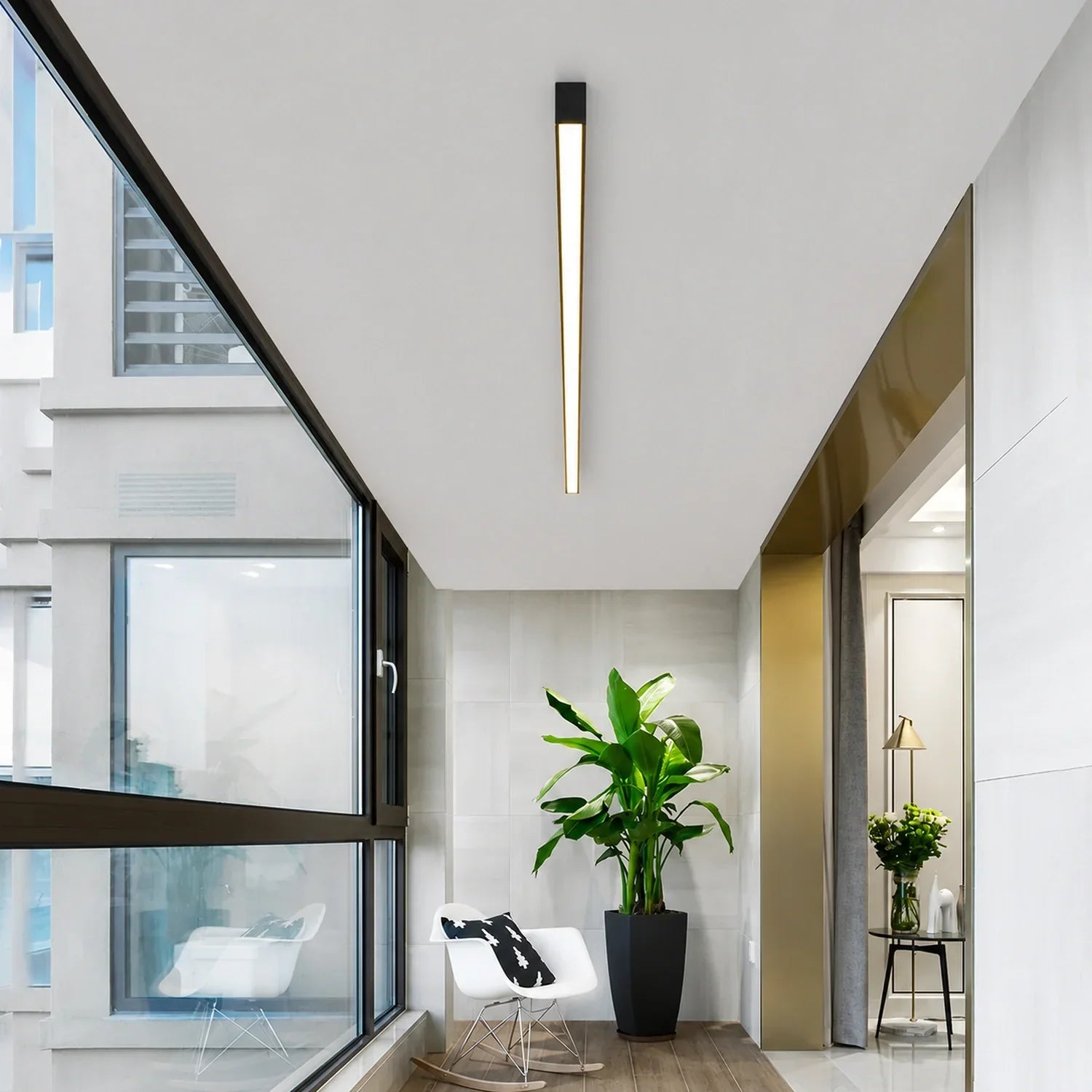 A minimalist linear LED ceiling light installed in a modern sunroom with a white rocking chair, large potted plant and floor-to-ceiling windows.