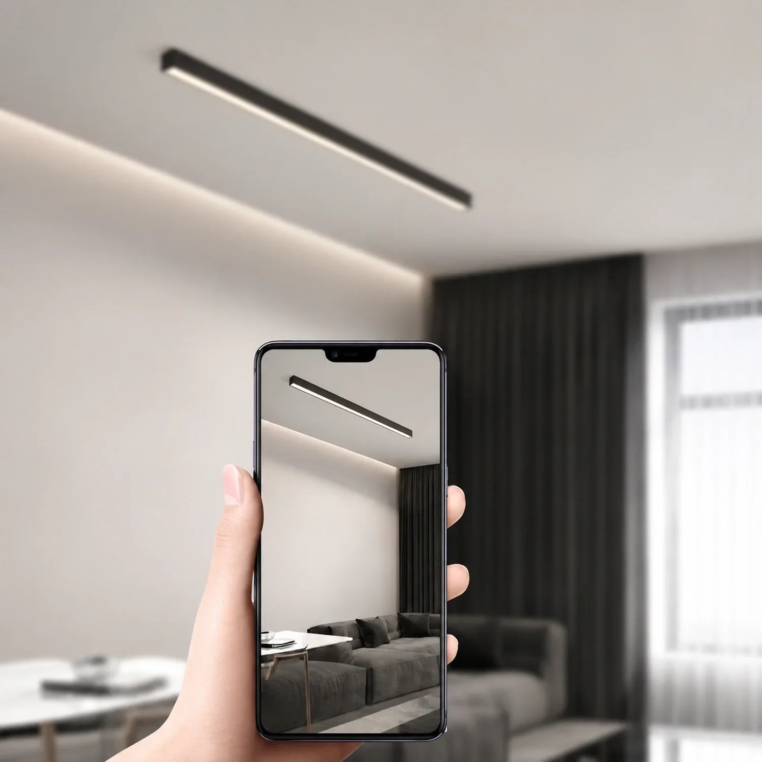 A hand holding a smartphone displaying a minimalist linear LED ceiling light installed in a modern living room with dark curtains and contemporary decor.