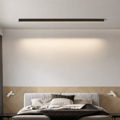 Minimalist black linear LED ceiling light mounted above a modern bedroom bed, casting a warm glow against the white wall and wooden headboard.