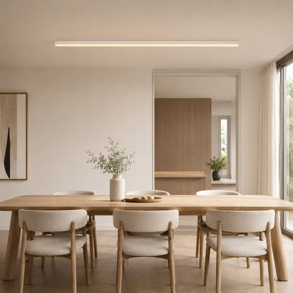 A minimalist white linear LED ceiling light mounted above a wooden dining table in a modern, neutral-toned interior living space.