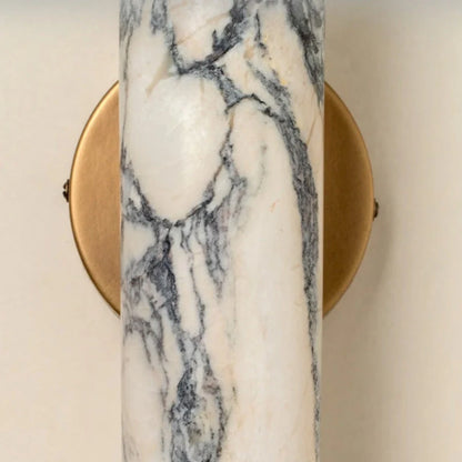 Close-up of a minimalist wall lamp featuring a cylindrical white marble shade with grey veining mounted on a circular brushed brass base.
