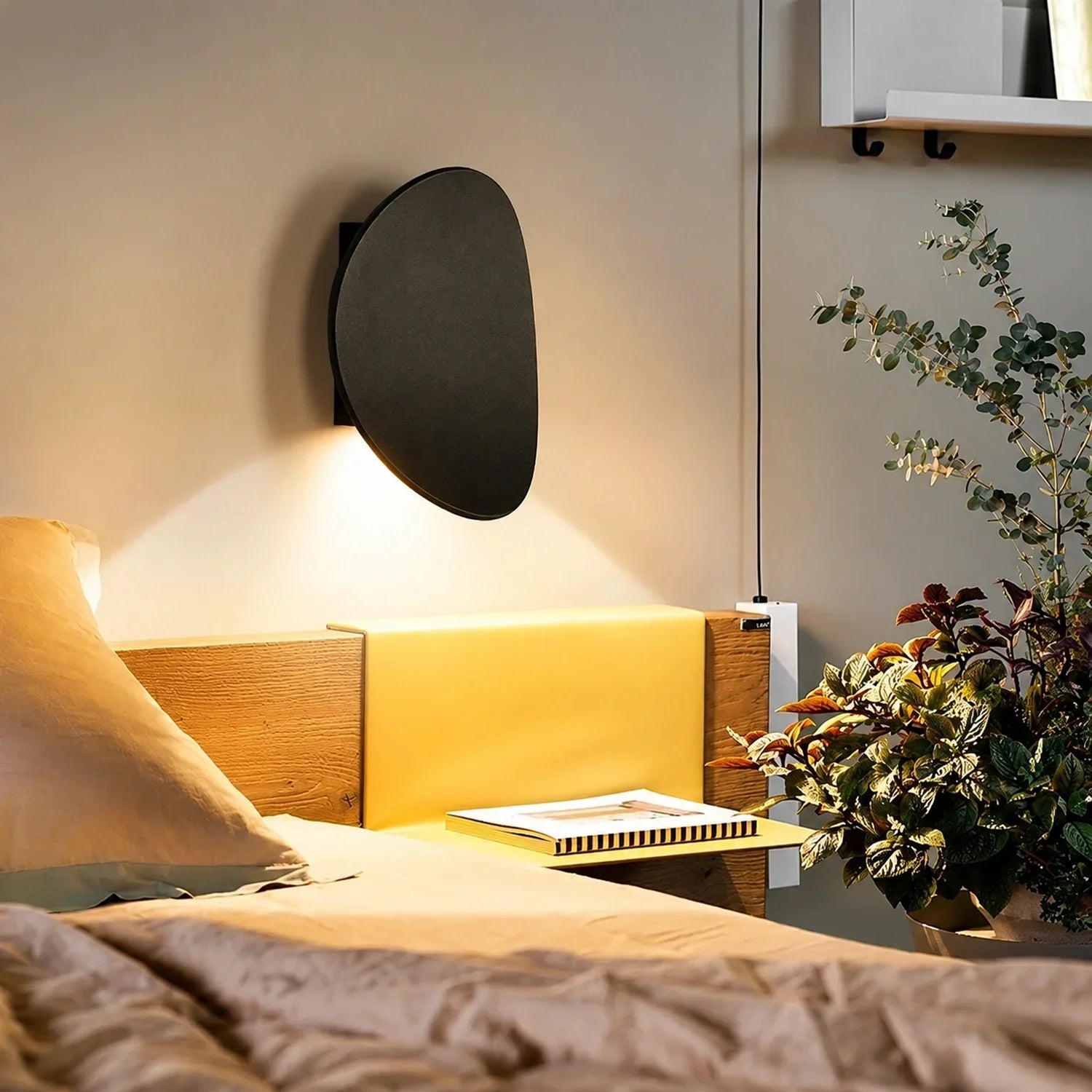 A modern black curved aluminium LED wall light mounted above a wooden bedside table, casting a warm, soft glow against a neutral bedroom wall.