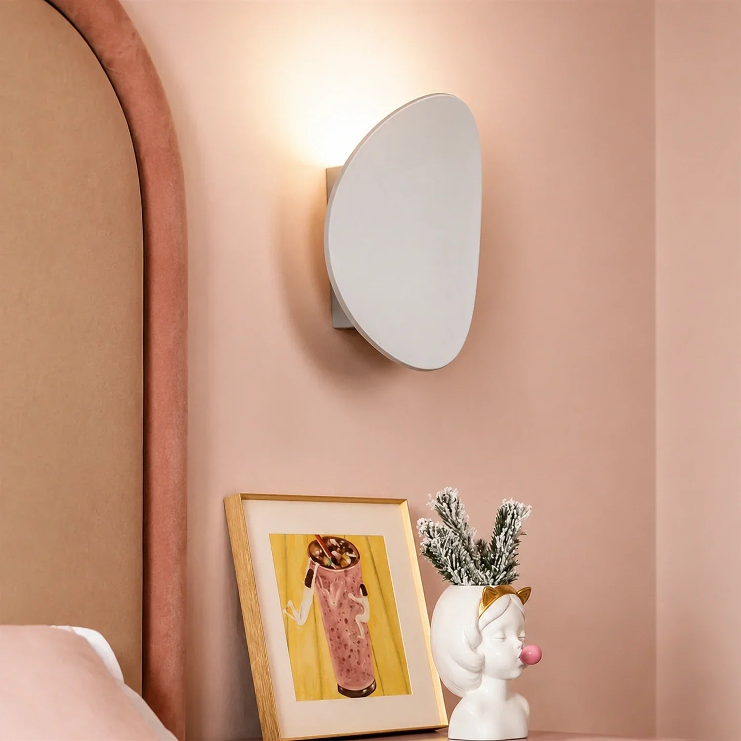 Modern white aluminium LED wall light mounted on a soft pink bedroom wall, providing warm up and down illumination above a framed print and decorative vase