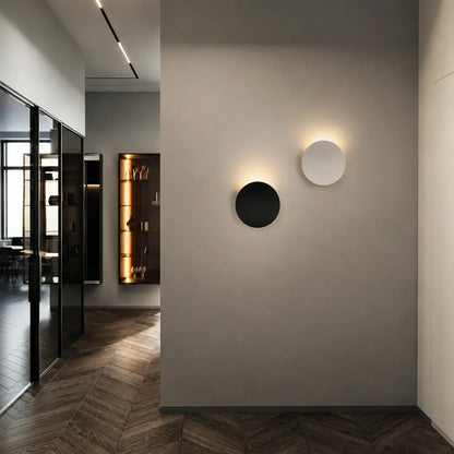 Two circular modern aluminium LED wall lights mounted on a grey interior wall, featuring soft up and down illumination in a contemporary hallway.