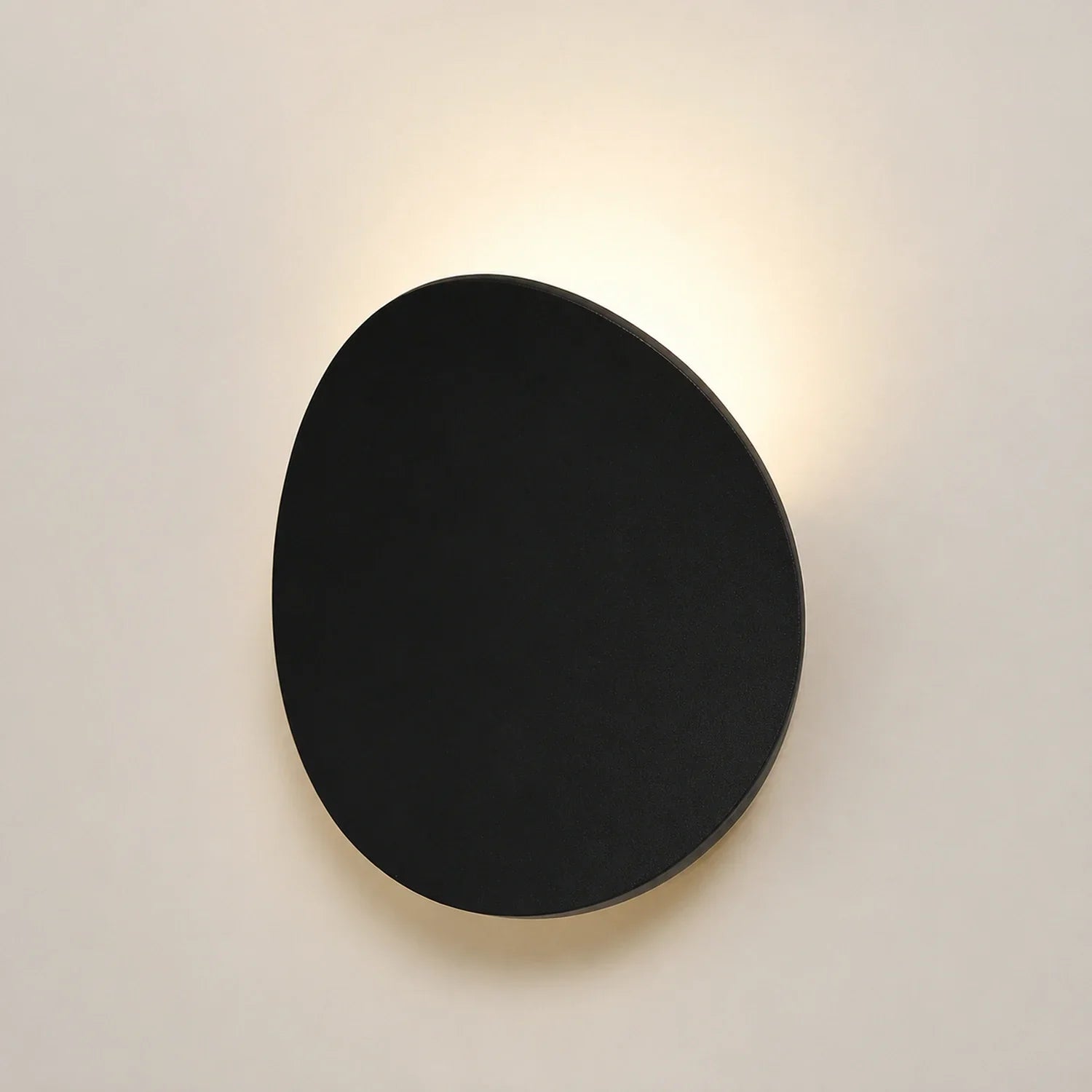 Modern black circular LED wall light mounted on a neutral wall, casting a soft, warm glow from the top and bottom edges for a stylish ambient effect.