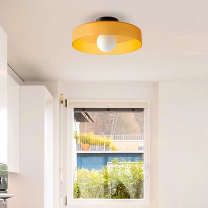 Modern Bauhaus flush mount ceiling light with a vibrant yellow circular shade and central white globe bulb, installed in a bright, minimalist kitchen.
