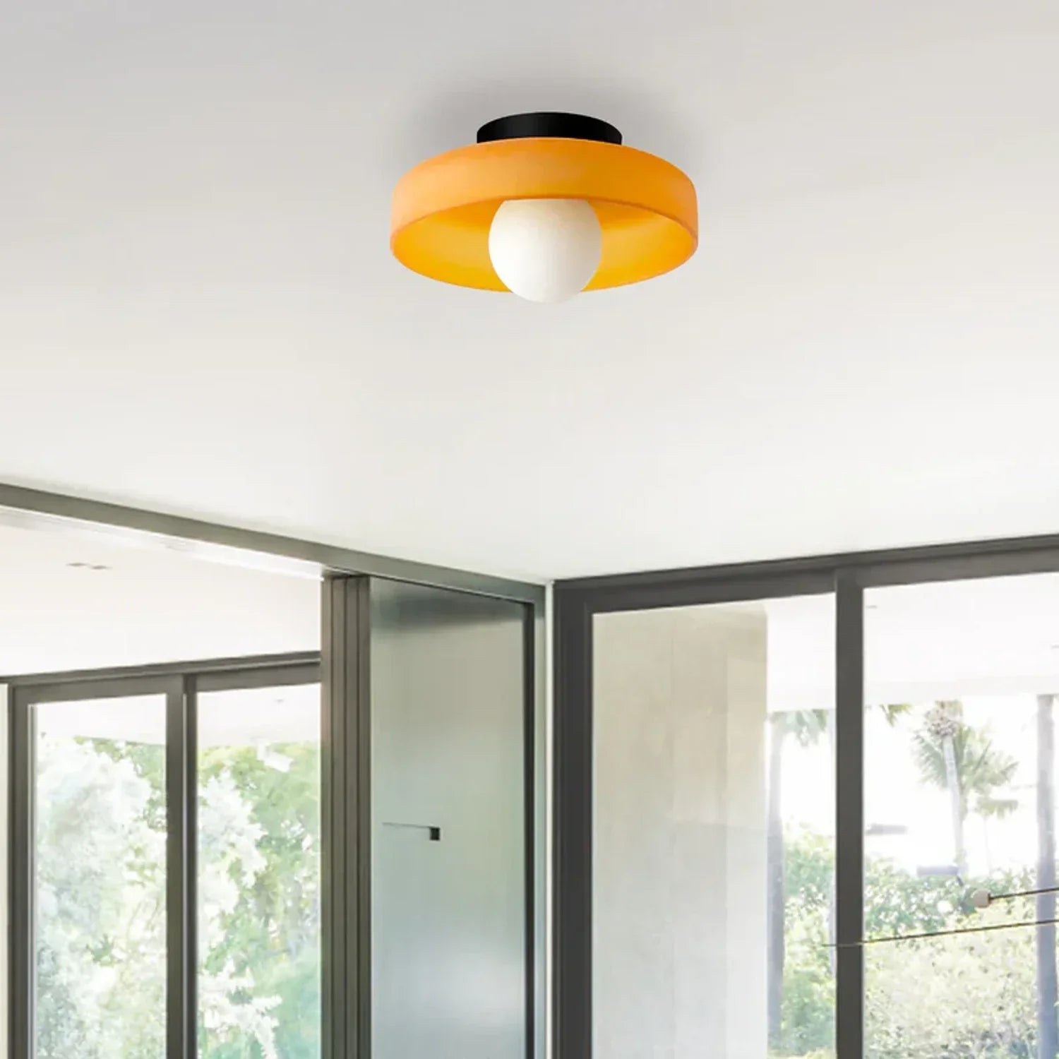Modern Bauhaus flush mount ceiling light featuring a vibrant orange circular shade and a central white glass bulb, installed in a contemporary room.