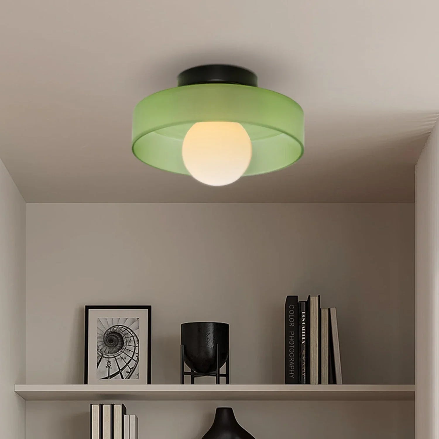 Modern Bauhaus style flush mount ceiling light featuring a green glass shade and a glowing central bulb, mounted on a neutral interior ceiling.