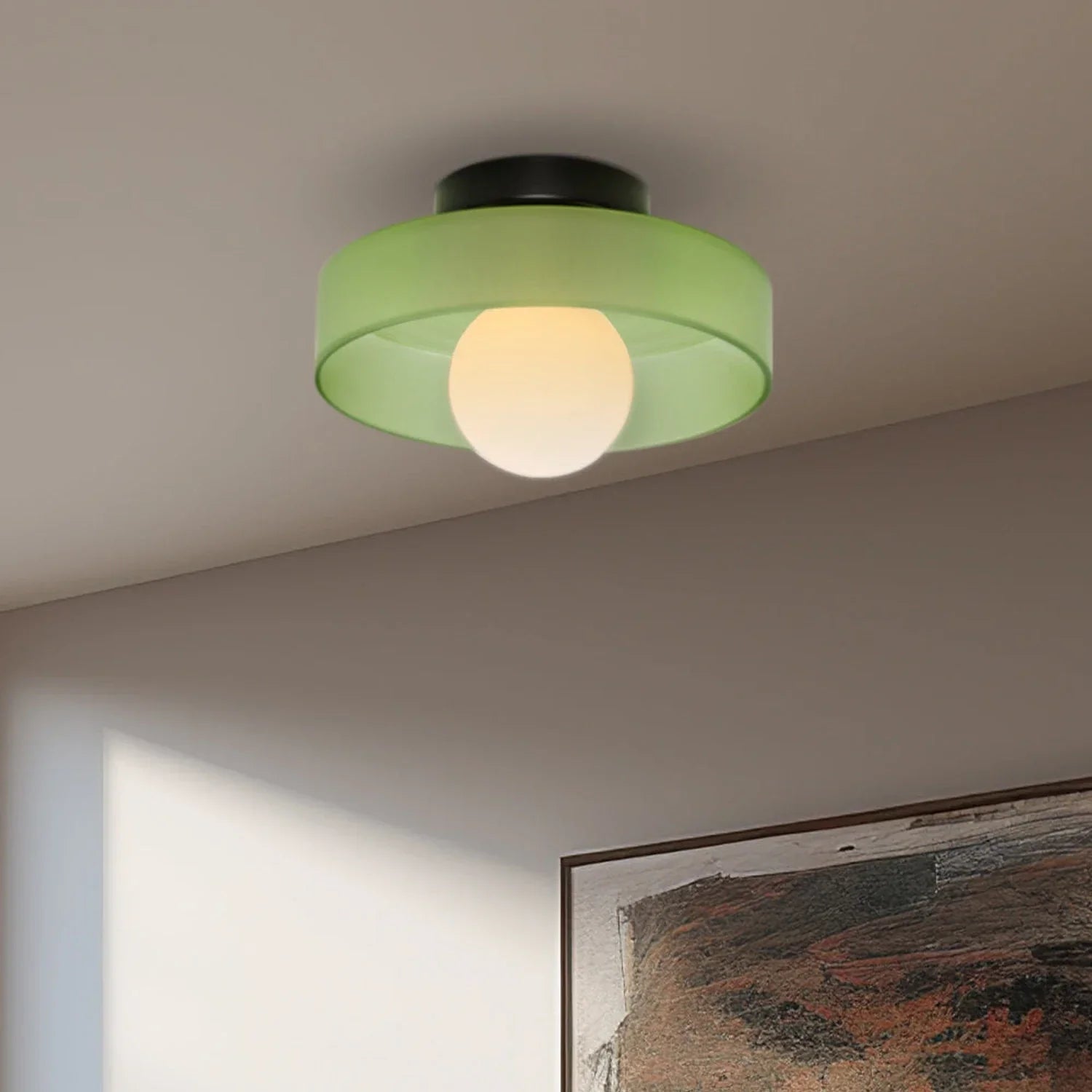 Modern Bauhaus style flush mount ceiling light featuring a circular green glass shade and a central glowing bulb mounted on a black iron base.