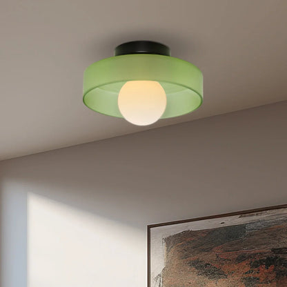 Modern Bauhaus style flush mount ceiling light featuring a circular green glass shade and a central glowing bulb mounted on a black iron base.