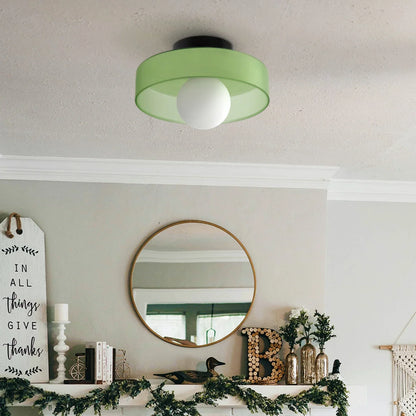 Modern Bauhaus flush mount ceiling light with a sage green drum shade and a central white globe bulb, installed in a stylish living room interior.