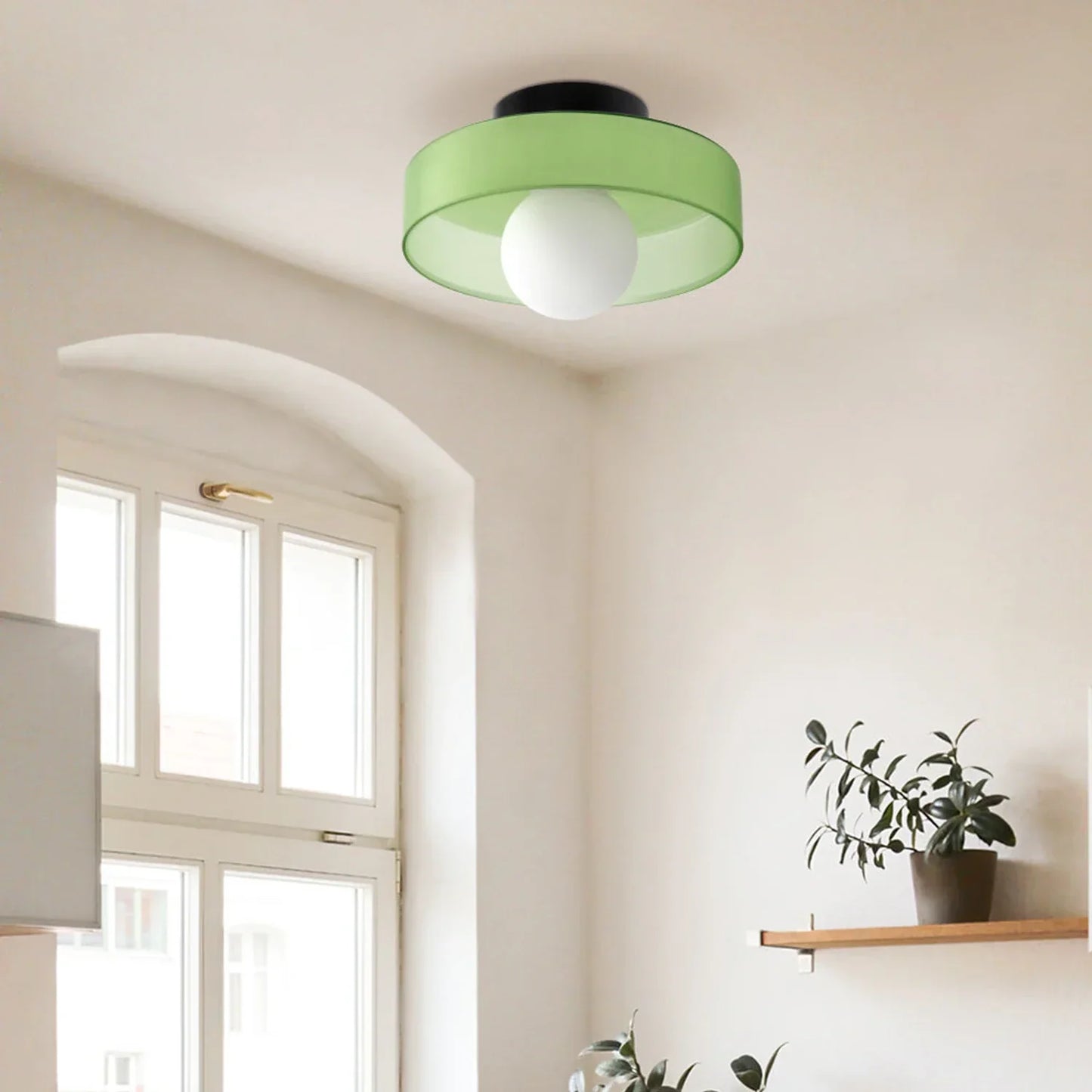 Modern Bauhaus flush mount ceiling light with a vibrant green shade and central white glass globe, installed in a bright room with a window and shelf.