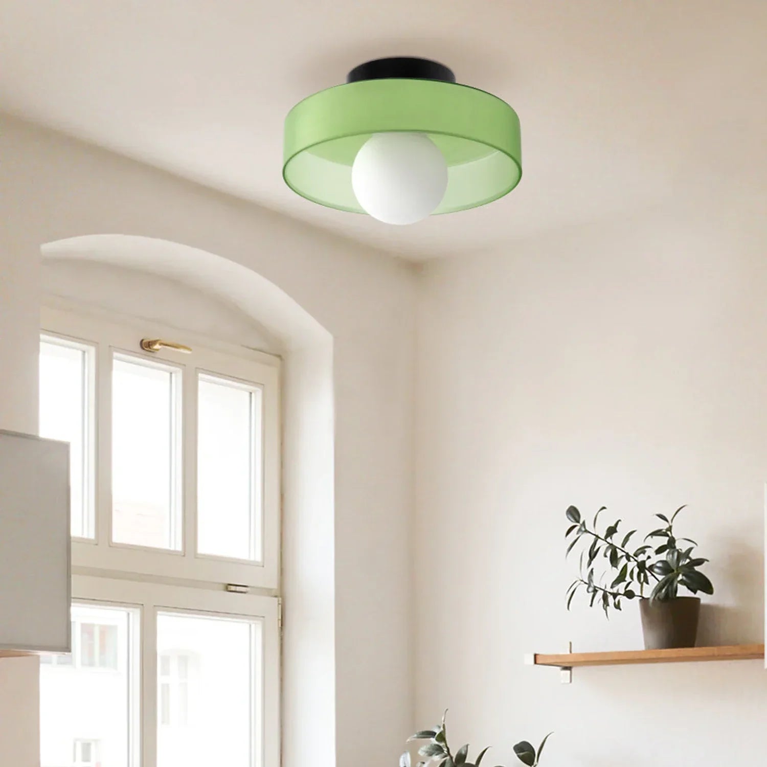 Modern Bauhaus flush mount ceiling light with a vibrant green shade and central white glass globe, installed in a bright room with a window and shelf.