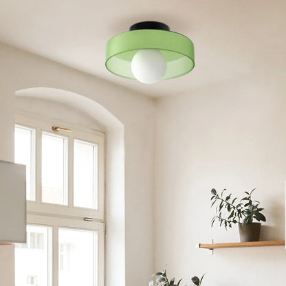 Modern Bauhaus flush mount ceiling light with a vibrant green shade and central white glass globe, installed in a bright room with a window and shelf.
