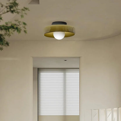 Modern Bauhaus style flush mount ceiling light with a wide olive green glass shade and a central white globe bulb, installed in a neutral interior.