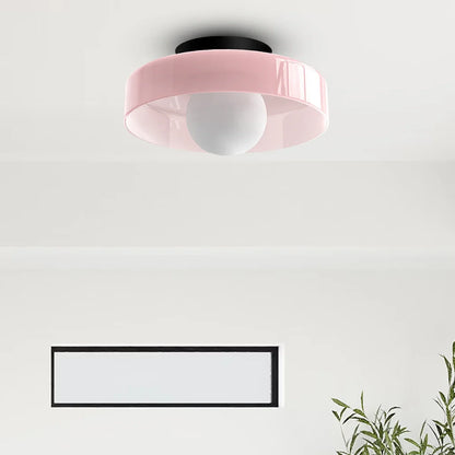 Modern Bauhaus flush mount ceiling light featuring a soft pink circular shade with a central white globe bulb, mounted on a black base in a room.