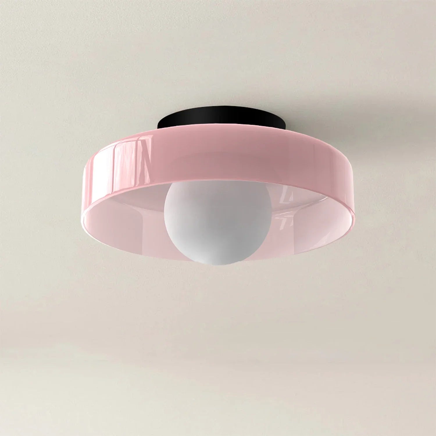 Modern Bauhaus flush mount ceiling light featuring a soft pink circular glass shade and a central white globe bulb against a neutral ceiling.