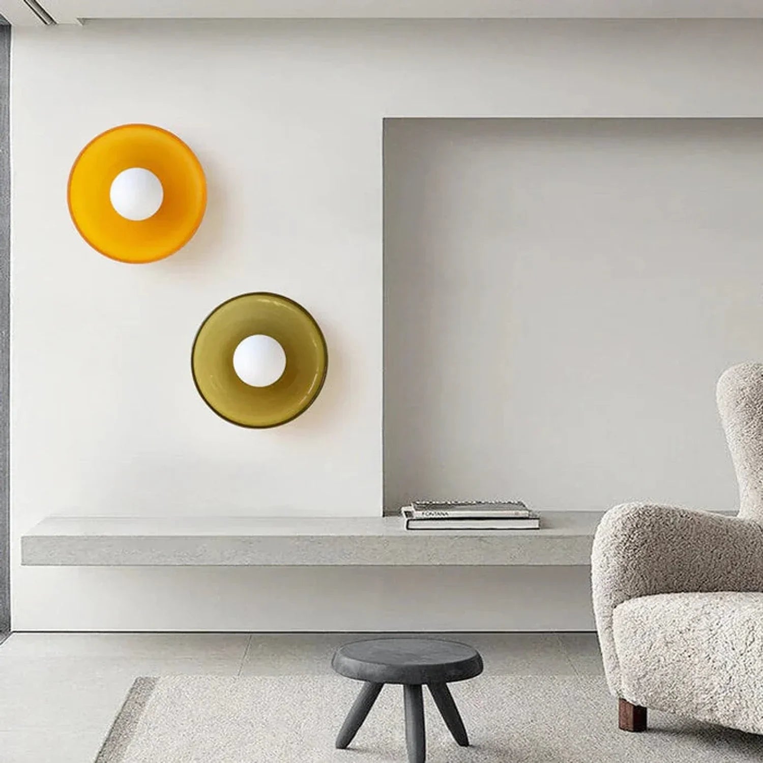 Two circular Bauhaus style flush mount wall lights with vibrant orange and green glass shades and white bulbs mounted on a minimalist interior wall.