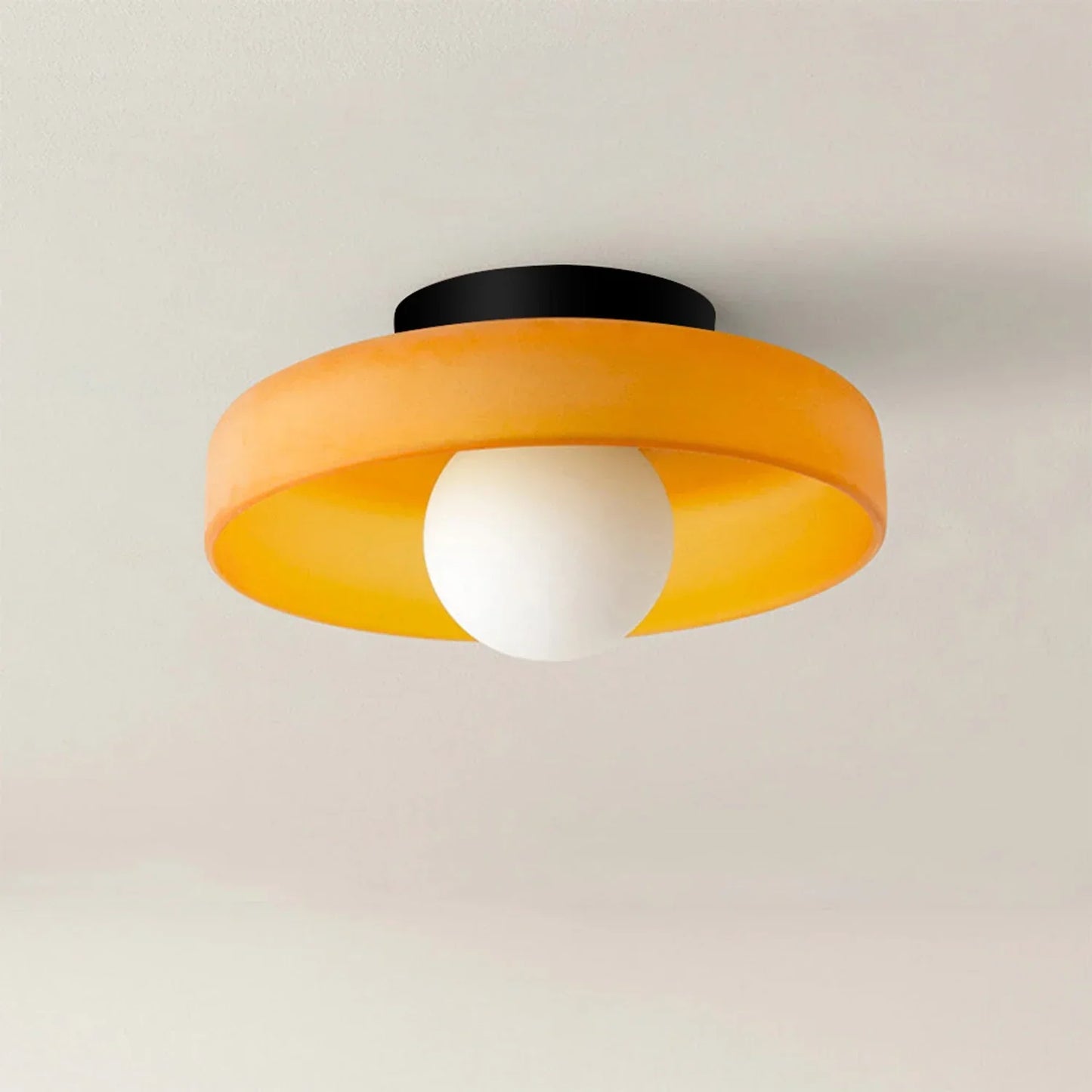 Modern Bauhaus flush mount ceiling light featuring a vibrant orange glass shade and a central white globe bulb mounted on a black iron base.