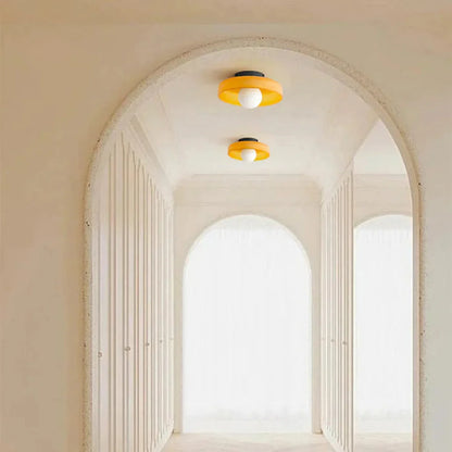 Two modern Bauhaus-style flush mount ceiling lights with orange circular shades and white globe bulbs installed in a bright, arched hallway interior.