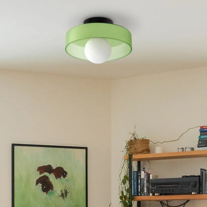 Modern Bauhaus style flush mount ceiling light featuring a frosted green glass shade and a central white globe bulb, mounted in a contemporary room.