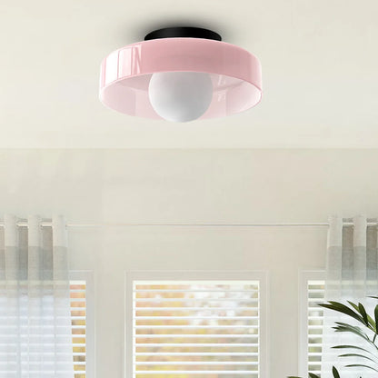 Modern Bauhaus style flush mount ceiling light featuring a pink circular shade and a central white glass globe bulb, mounted on a white ceiling.
