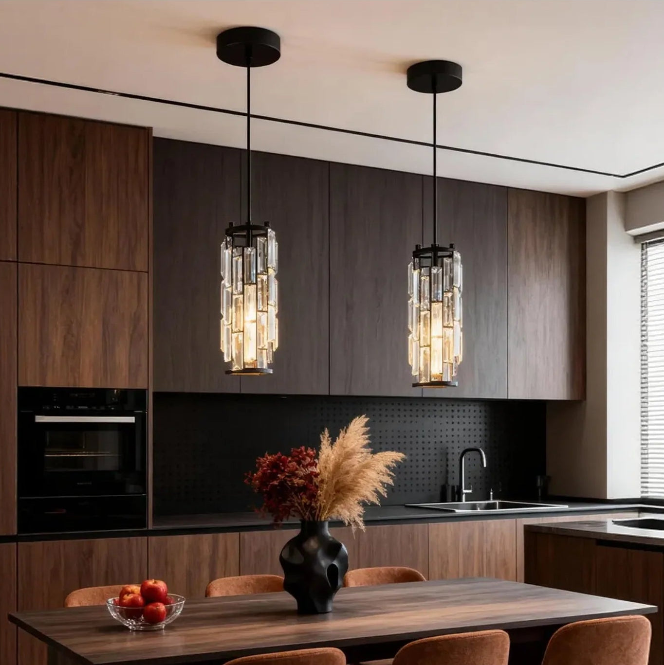 Two modern crystal pendant lights with black cords hanging over a wooden dining table, providing warm illumination in a stylish kitchen sett
