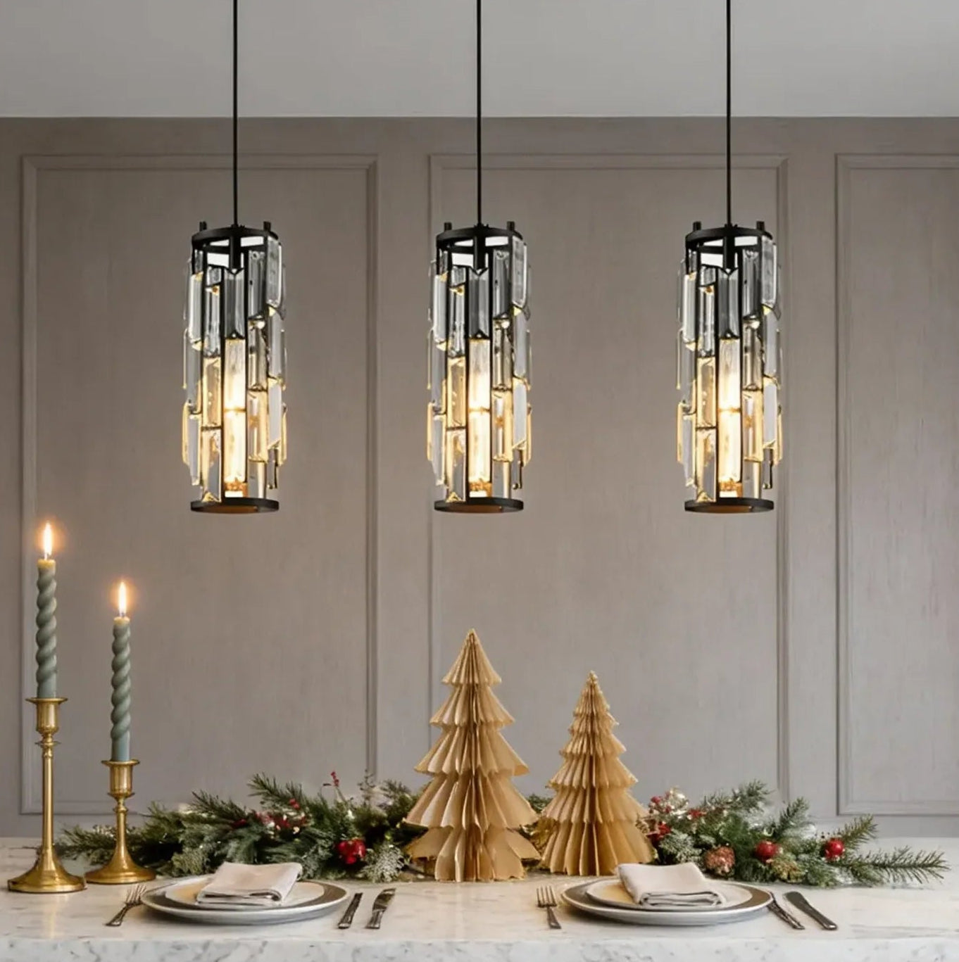 Three modern crystal pendant lights with adjustable cords hanging over a festive dining table decorated with candles and paper Christmas tre