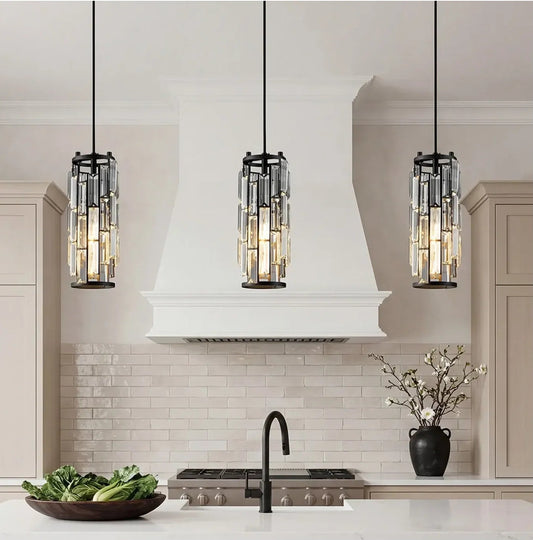 Three modern crystal pendant lights with black frames and adjustable cords hanging over a kitchen island, providing warm, elegant kitchen li