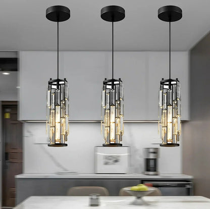 Three modern black crystal pendant lights with adjustable cords, emitting a warm glow in a row above a contemporary kitchen counter.