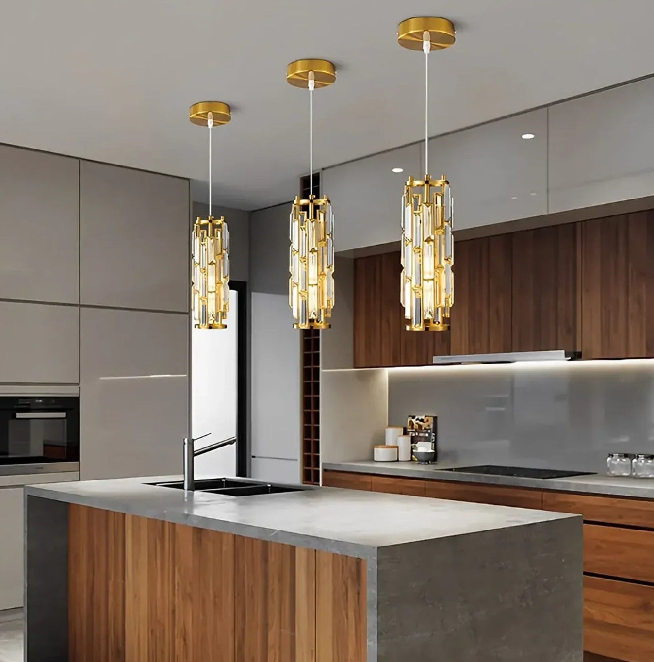 Three modern gold crystal pendant lights with warm light hanging over a contemporary kitchen island with a grey stone countertop.