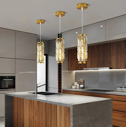 Three modern gold crystal pendant lights with warm light hanging over a contemporary kitchen island with a grey stone countertop.