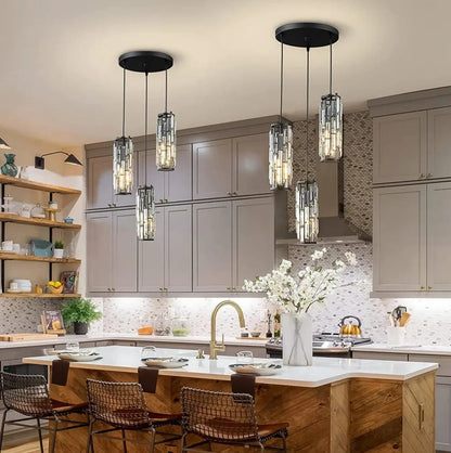 Two modern 3-light black crystal pendant lights with adjustable cords, casting a warm glow over a kitchen island with grey cabinets.
