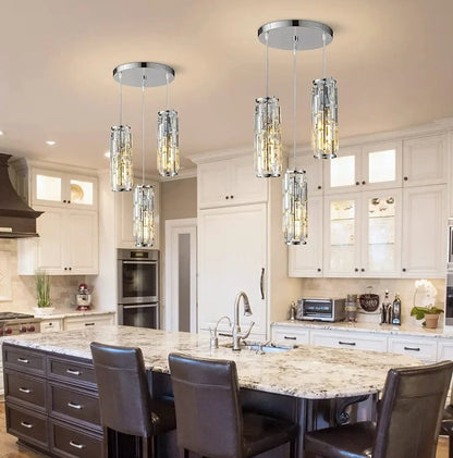Two modern 3-light chrome crystal pendant lights with warm illumination hanging above a kitchen island with marble countertops