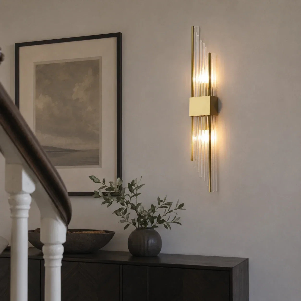Modern 35cm gold wall light with vertical crystal rods and warm illumination, mounted on a neutral interior wall above a dark wooden sideboard.