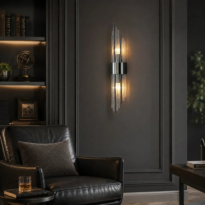 Modern crystal wall light with a black metal frame emitting a warm white glow, mounted on a dark panelled wall above a black leather armchair.