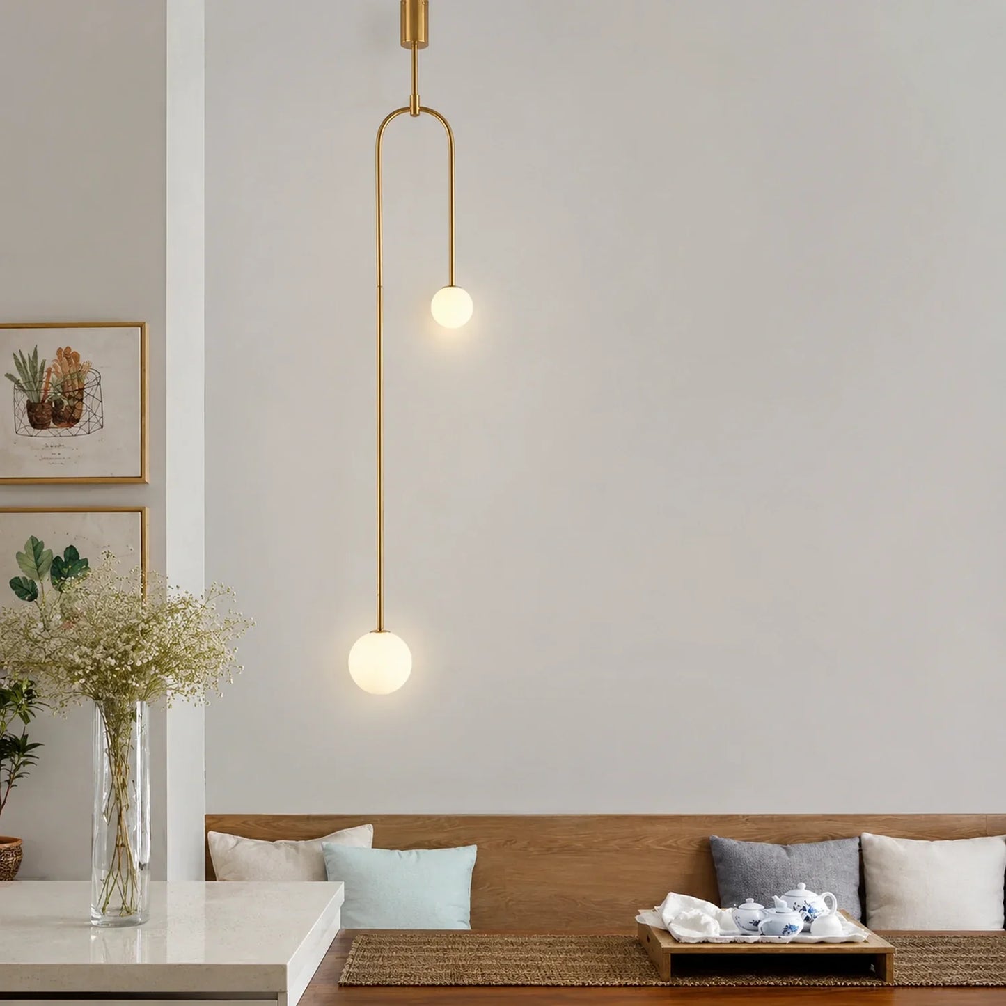 Modern double globe pendant light with a sleek gold finish suspended above a dining area with minimalist decor and soft ambient lighting.