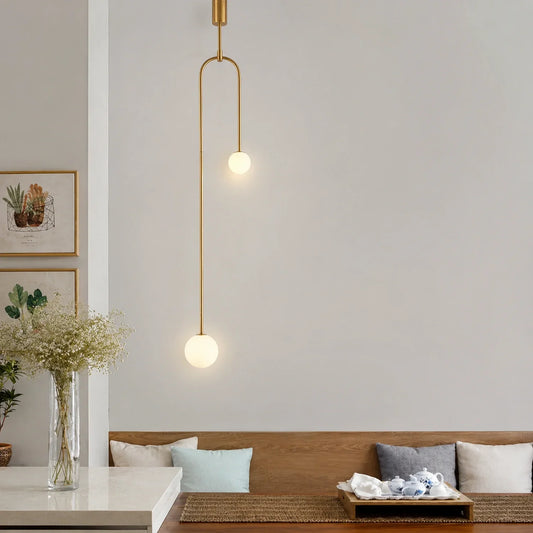 Modern double globe pendant light with a sleek gold finish suspended above a dining area with minimalist decor and soft ambient lighting.