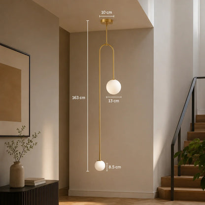 Modern gold double globe pendant light with dimensions shown, featuring two white spherical shades suspended in a minimalist interior hallway setting.