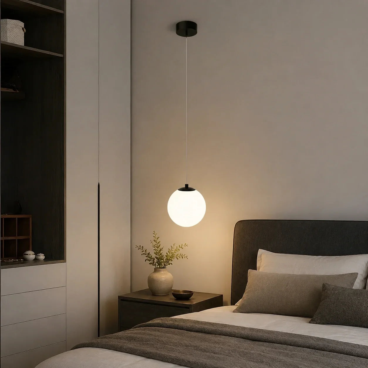 Modern glass globe pendant light with a black fixture hanging above a bedside table in a contemporary bedroom interior.