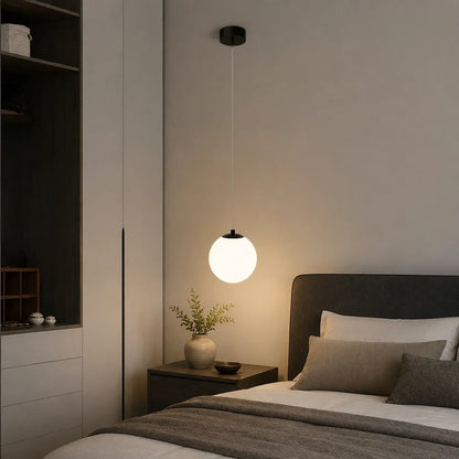 Modern glass globe pendant light with a black fixture hanging above a bedside table in a contemporary bedroom interior.