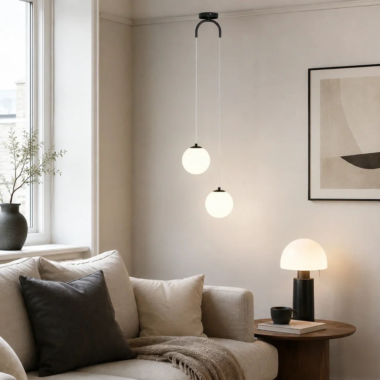 Modern glass globe pendant light with two glowing spheres hanging from a black ceiling mount in a contemporary living room with a neutral sofa.