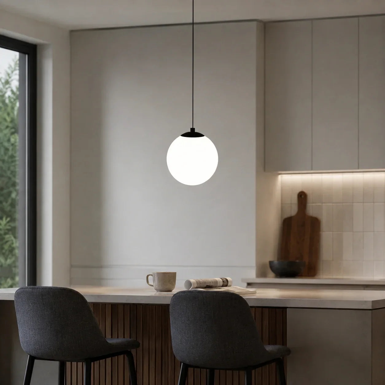 A modern glass globe pendant light with a black fixture hanging above a kitchen island in a contemporary home interior with grey upholstered chairs.