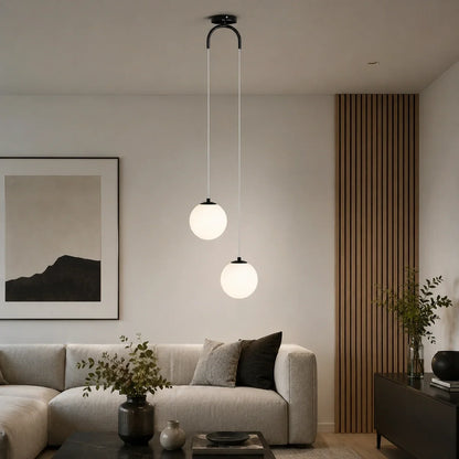 Modern ceiling pendant light featuring two glowing white glass globes suspended at different heights above a contemporary living room sofa.