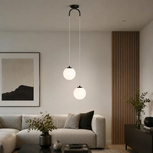Modern ceiling pendant light featuring two glowing white glass globes suspended at different heights above a contemporary living room sofa.